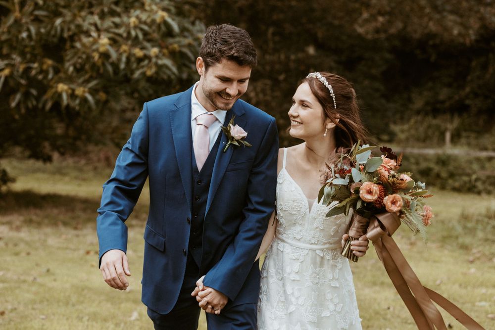 A couple shares a romantic moment outdoors, with the bride holding a beautiful autumn-colored bouquet.