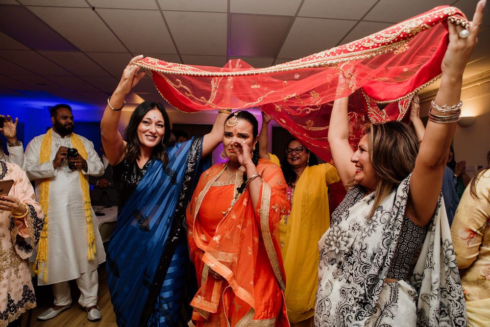Wedding celebration with traditional Indian attire and red dupatta being held up by dancing guests.