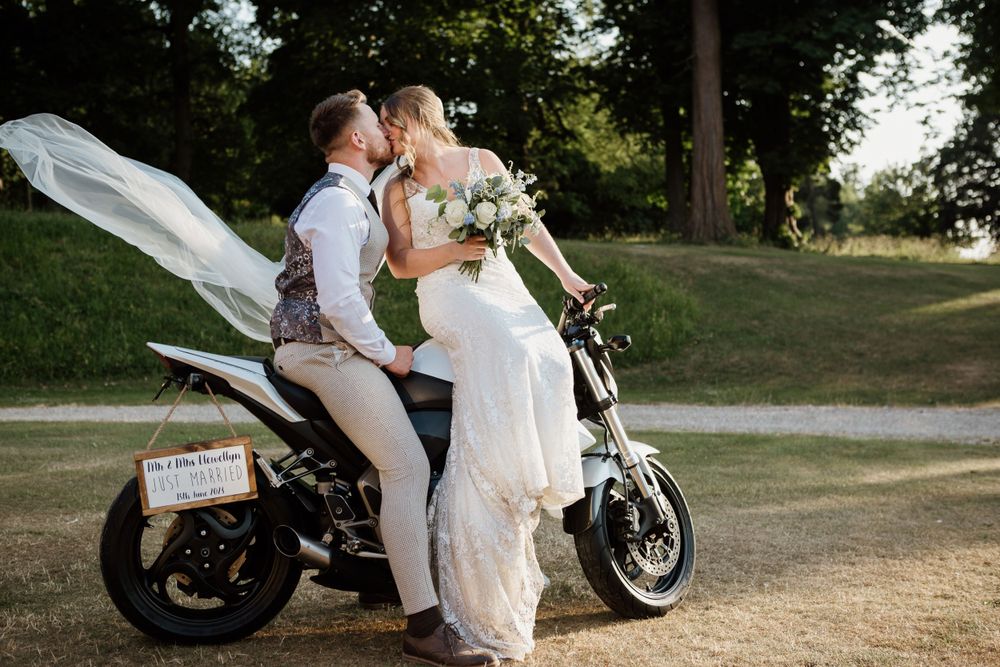 A couple shares a romantic moment on a motorcycle in formal wedding attire.