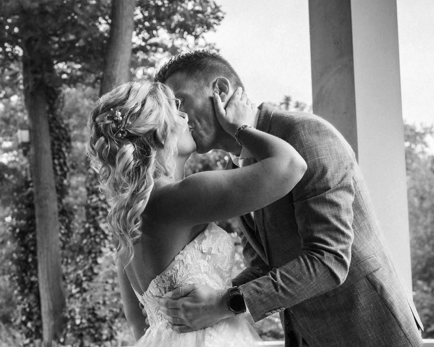 A romantic black and white portrait of a couple sharing an intimate moment under a columned porch.