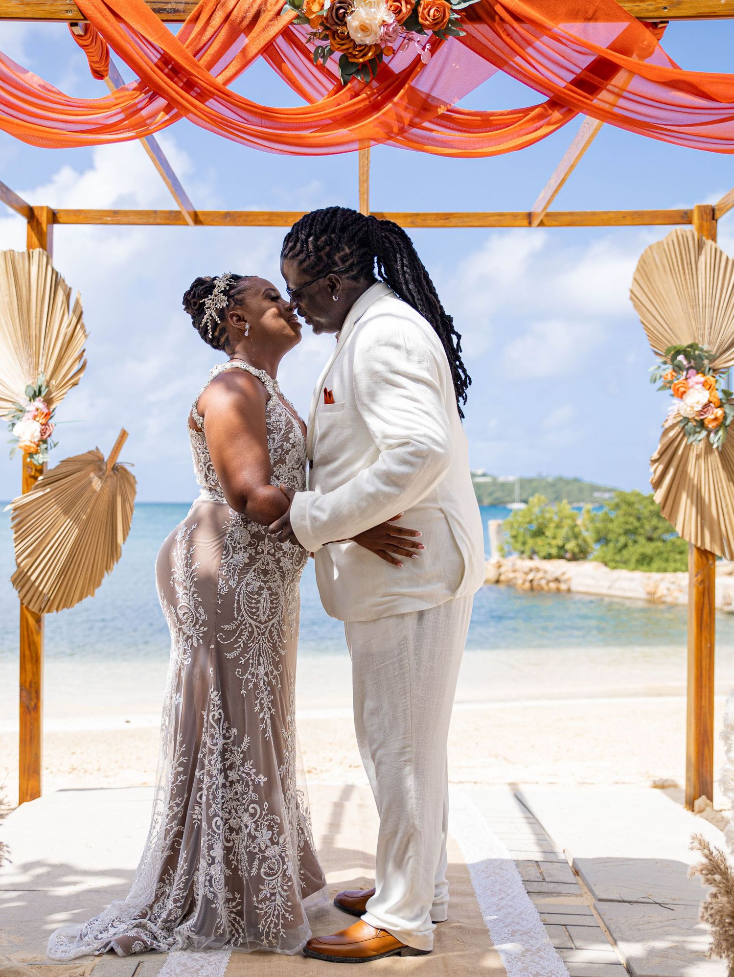 Wedding ceremony under an orange draped beach gazebo with palm leaf decor.