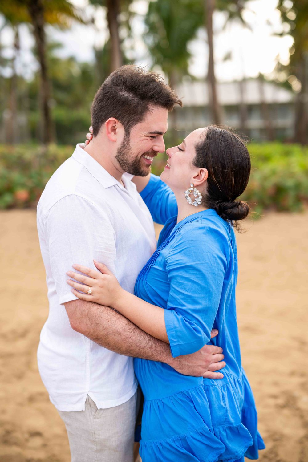 A romantic couple embraces while wearing coordinating white and blue outfits in a tropical setting.