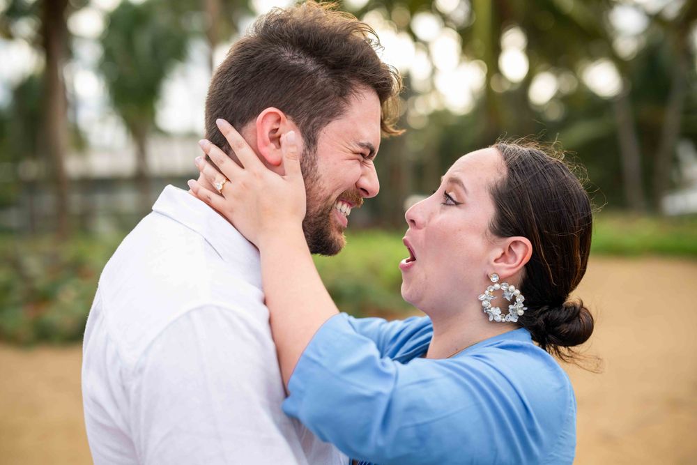 A joyful couple laughs together while sharing an intimate embrace in a garden setting.