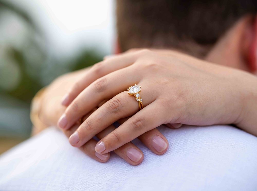 Close-up of an engagement ring on a hand resting on a white shirt.