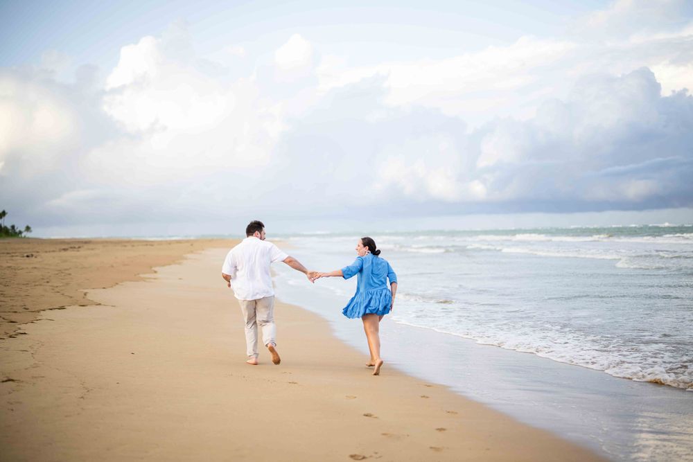 A couple runs playfully along the beach shore holding hands during a beautiful sunset.
