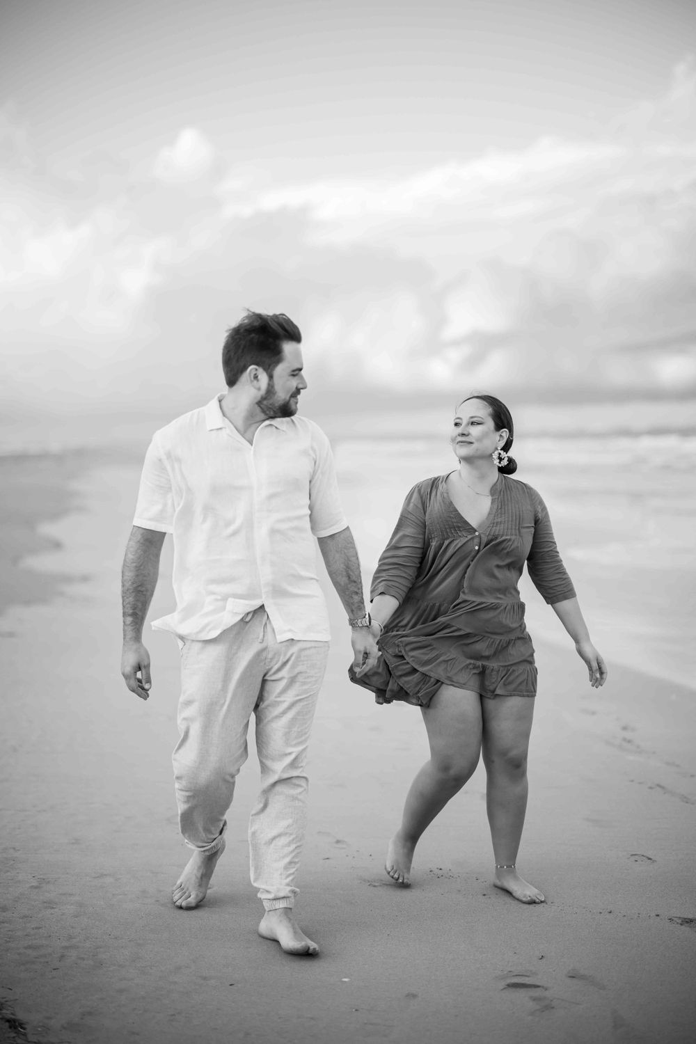Couple walking together playfully on a cloudy beach in black and white photo sequence.