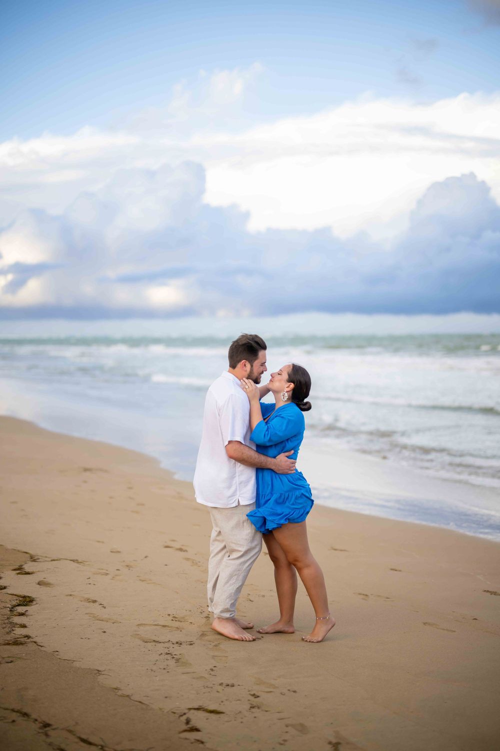 Couple embracing and dancing together on a scenic beach with rolling waves in the background.