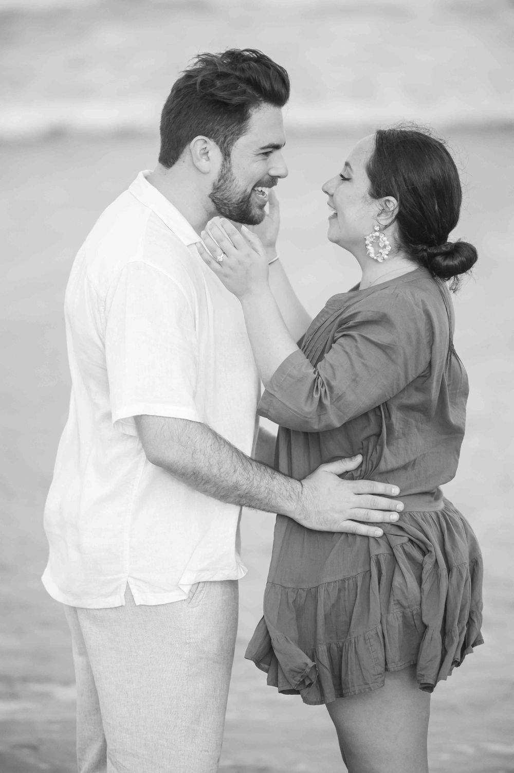 Sweet couple in casual attire sharing a tender moment on the beach in black and white.