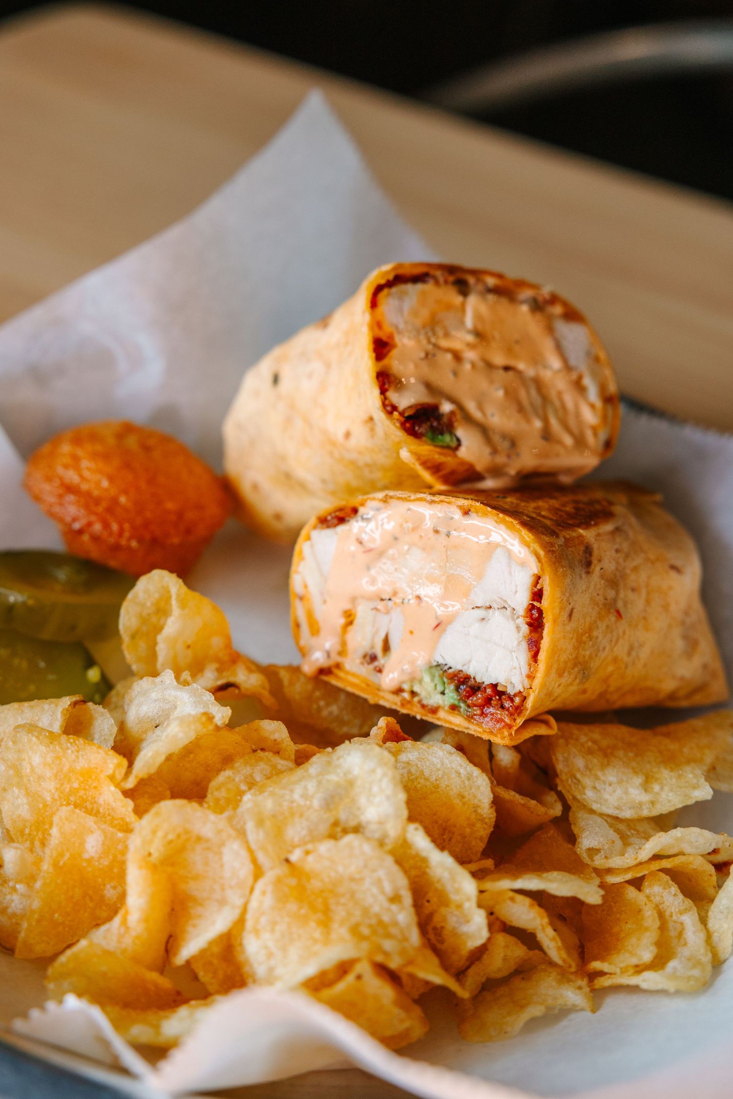 Wrap sandwich served with potato chips and pickles on parchment paper.