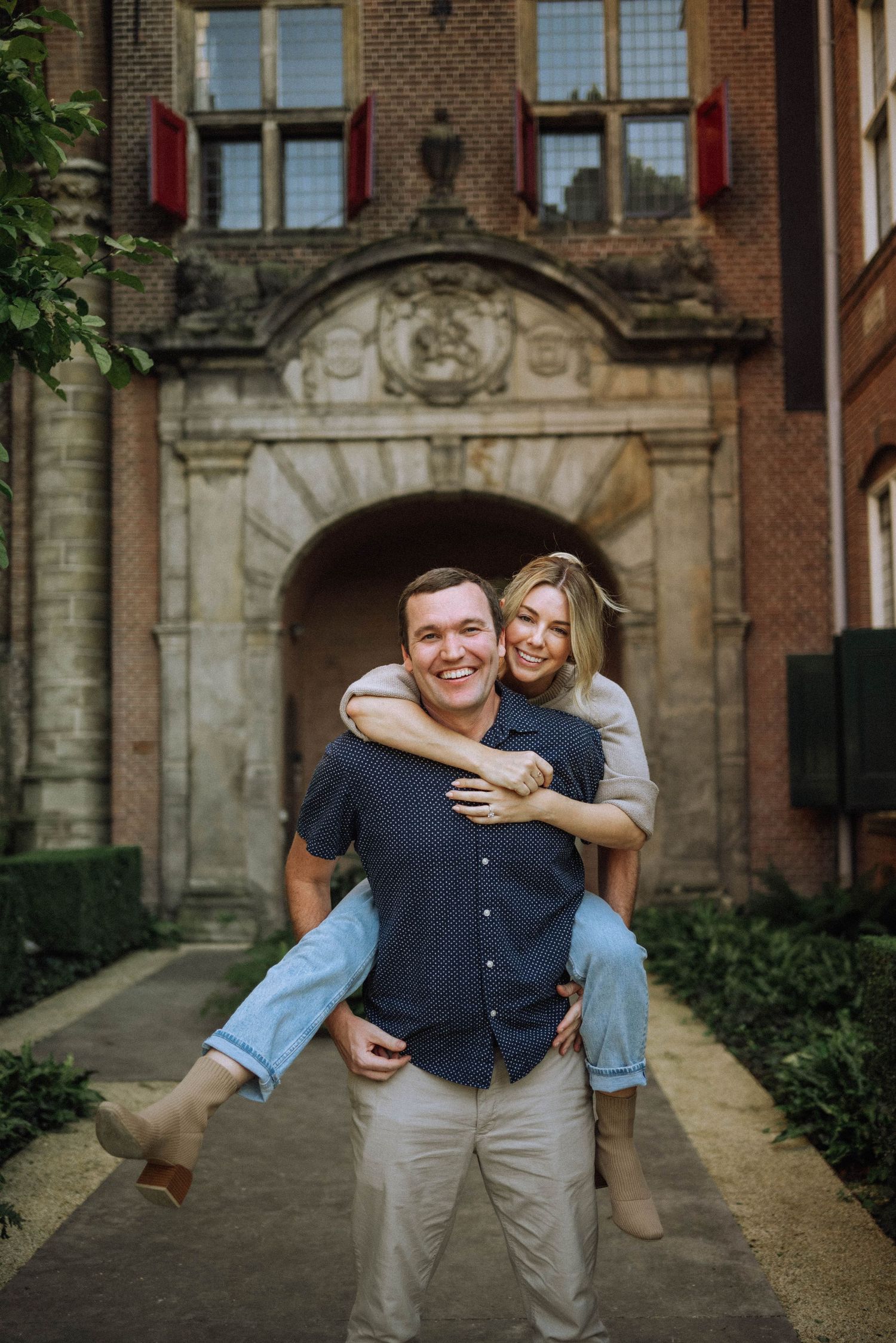 A joyful couple sharing a piggyback ride in front of an ornate brick building entrance.