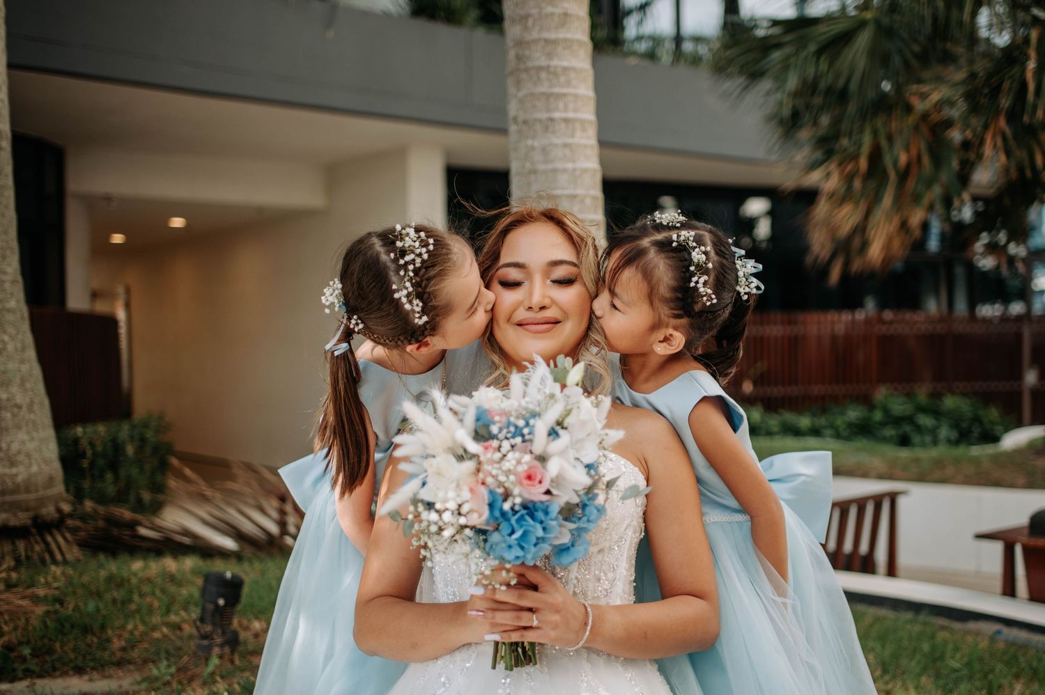 A bride in white holds a blue bouquet while being embraced.
