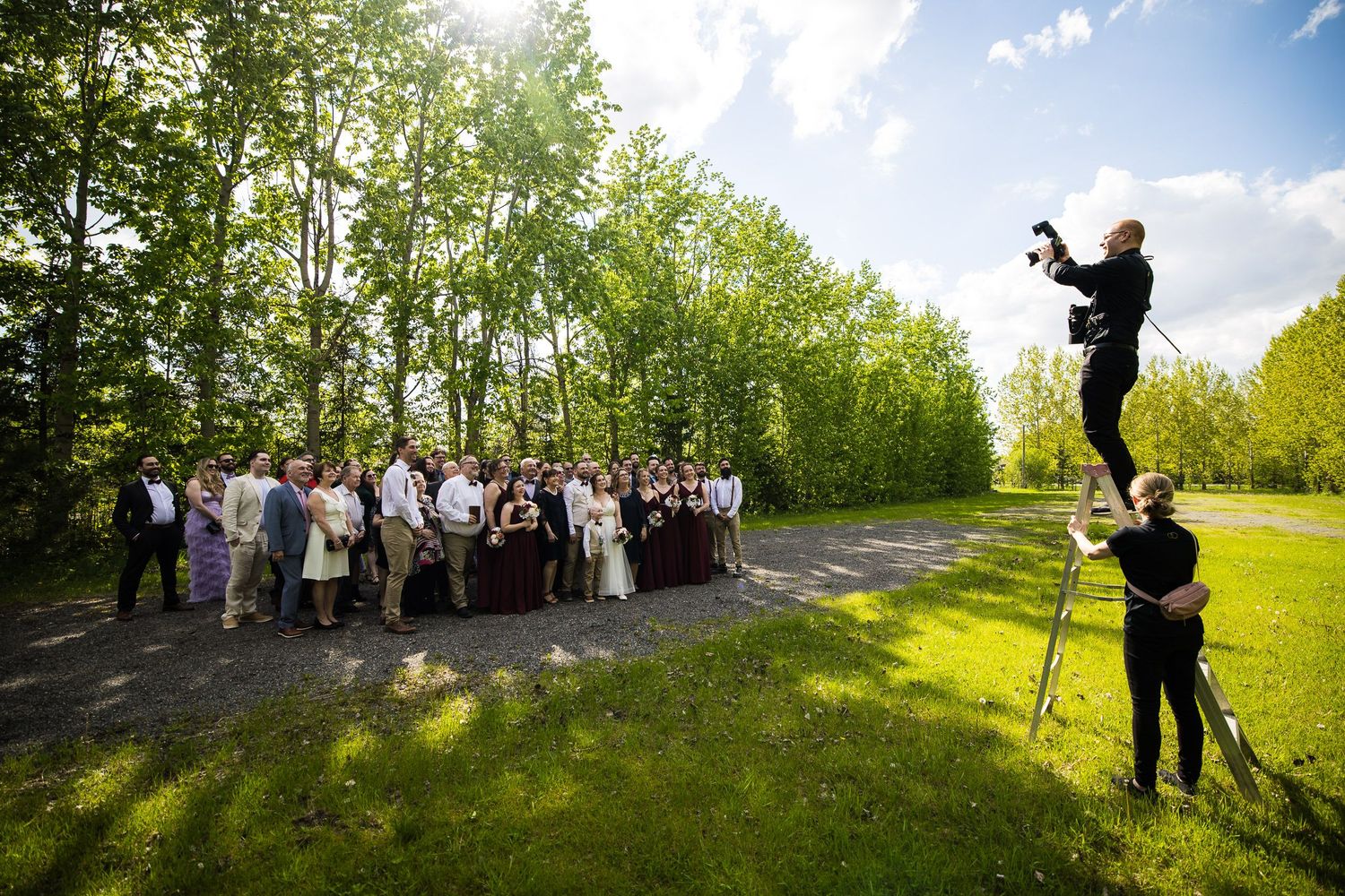 Photo du photographe Brophoto en plein travail durant un mariage. Il est debout sur un escabeau en train de photographier un grand groupe.