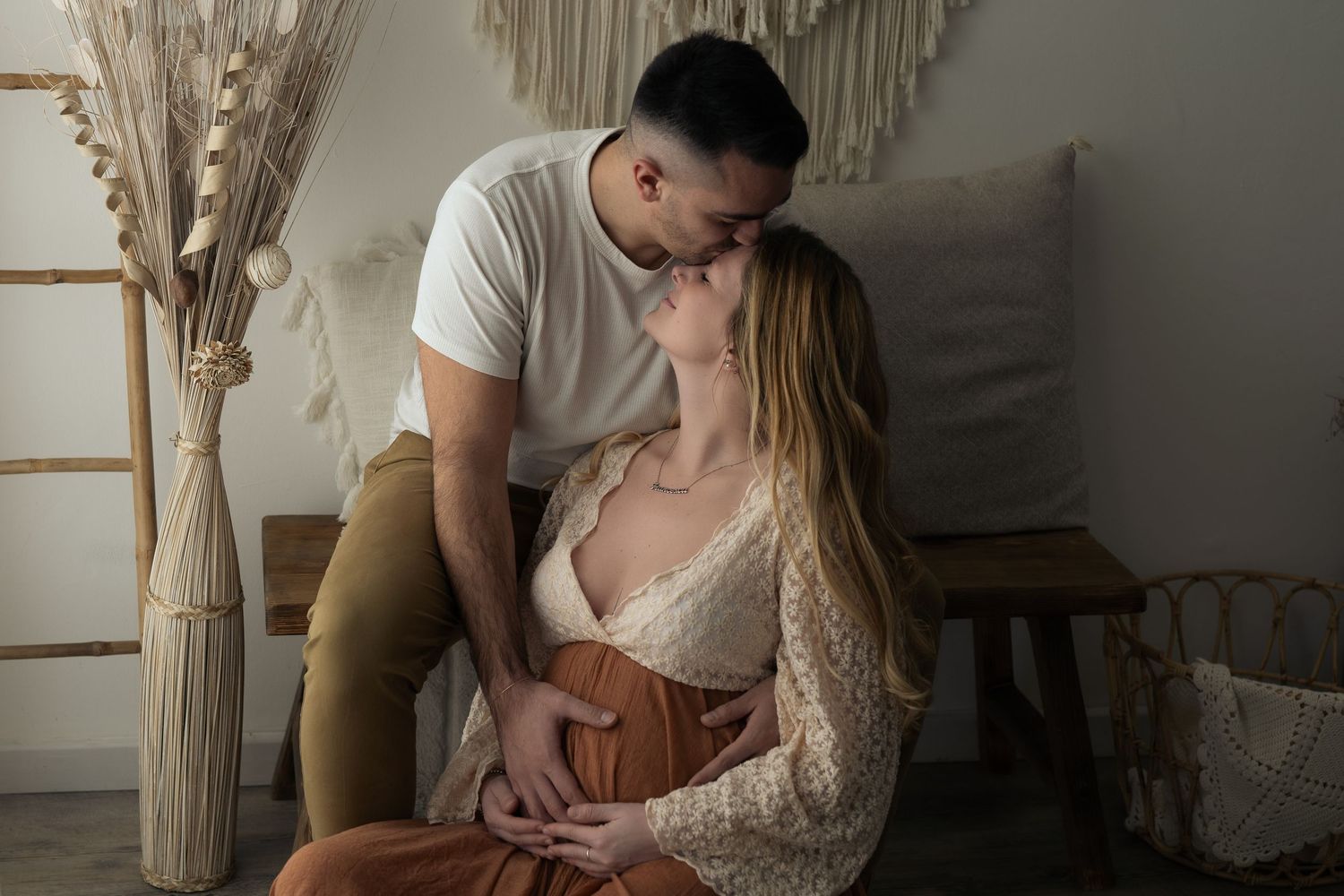 Coppia di futuri genitori si scambia un bacio all'interno di un set fotografico allestito in modo romantico con toni neutri