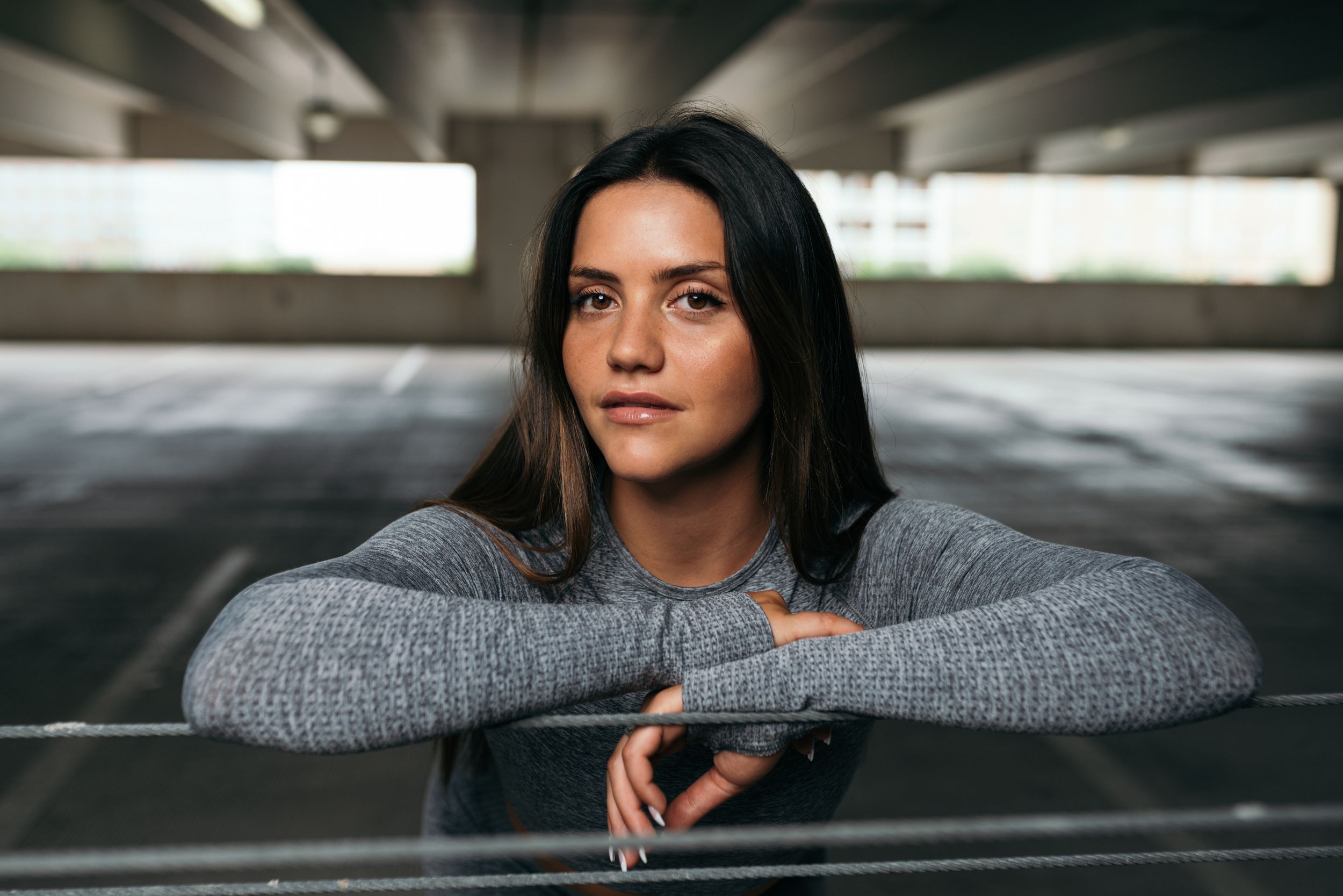 Portrait of person in gray sweater leaning on railing in dim parking structure.