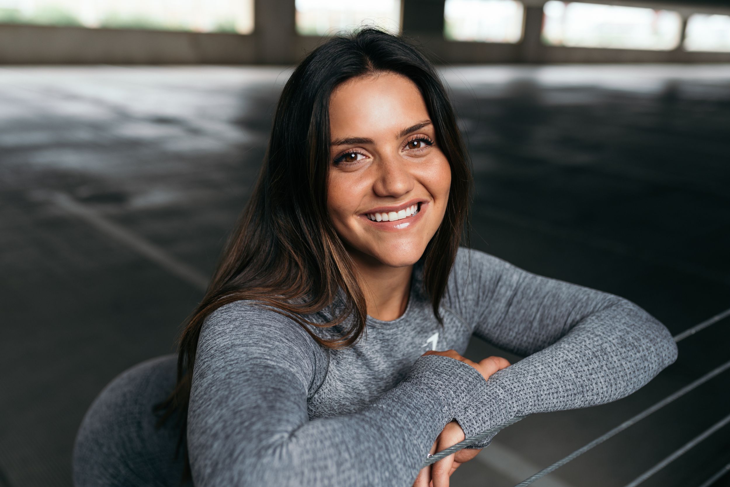 Casual portrait of person in gray sweater smiling in dimly lit indoor setting.