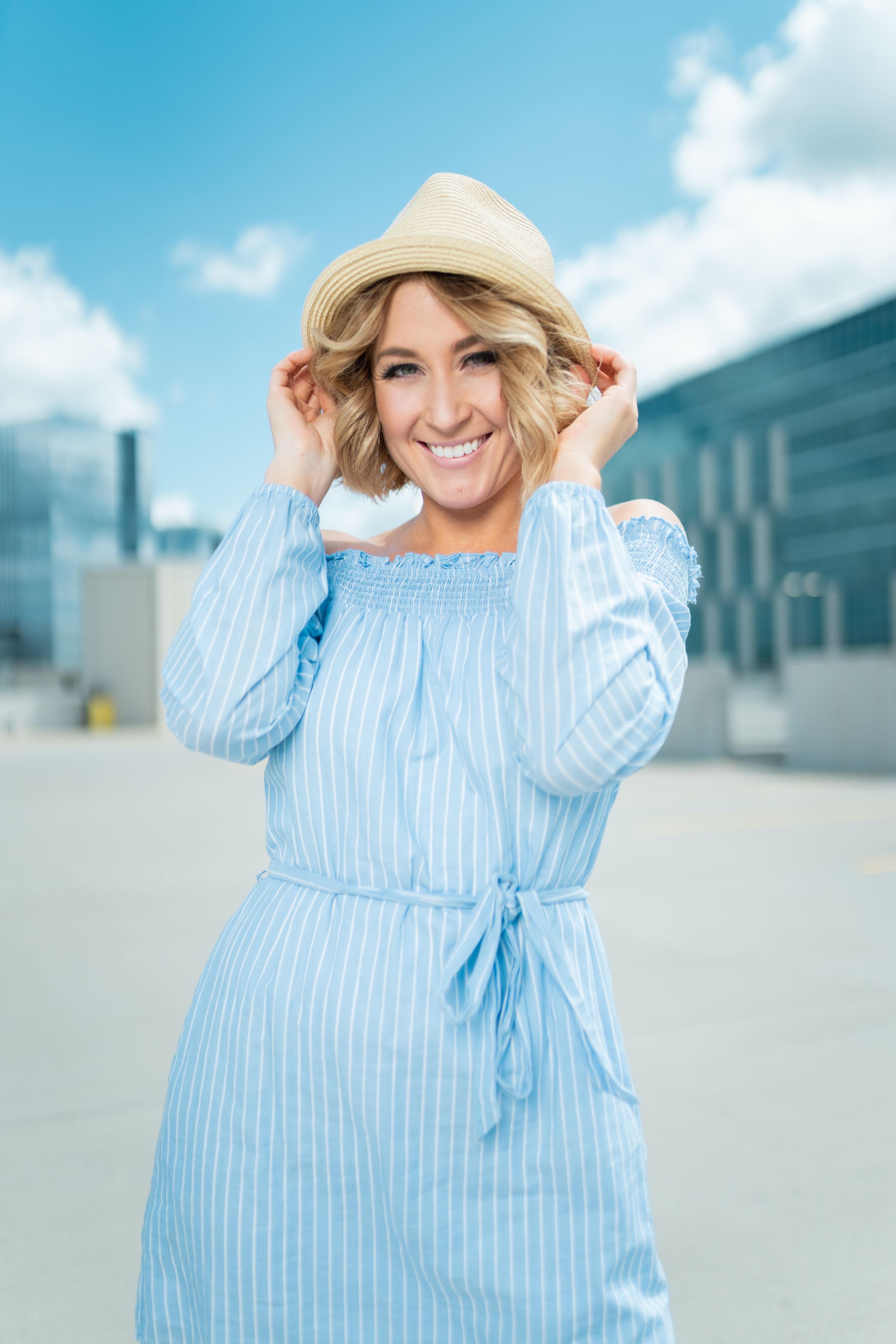 Woman in blue striped sundress and straw hat poses outdoors on sunny day.