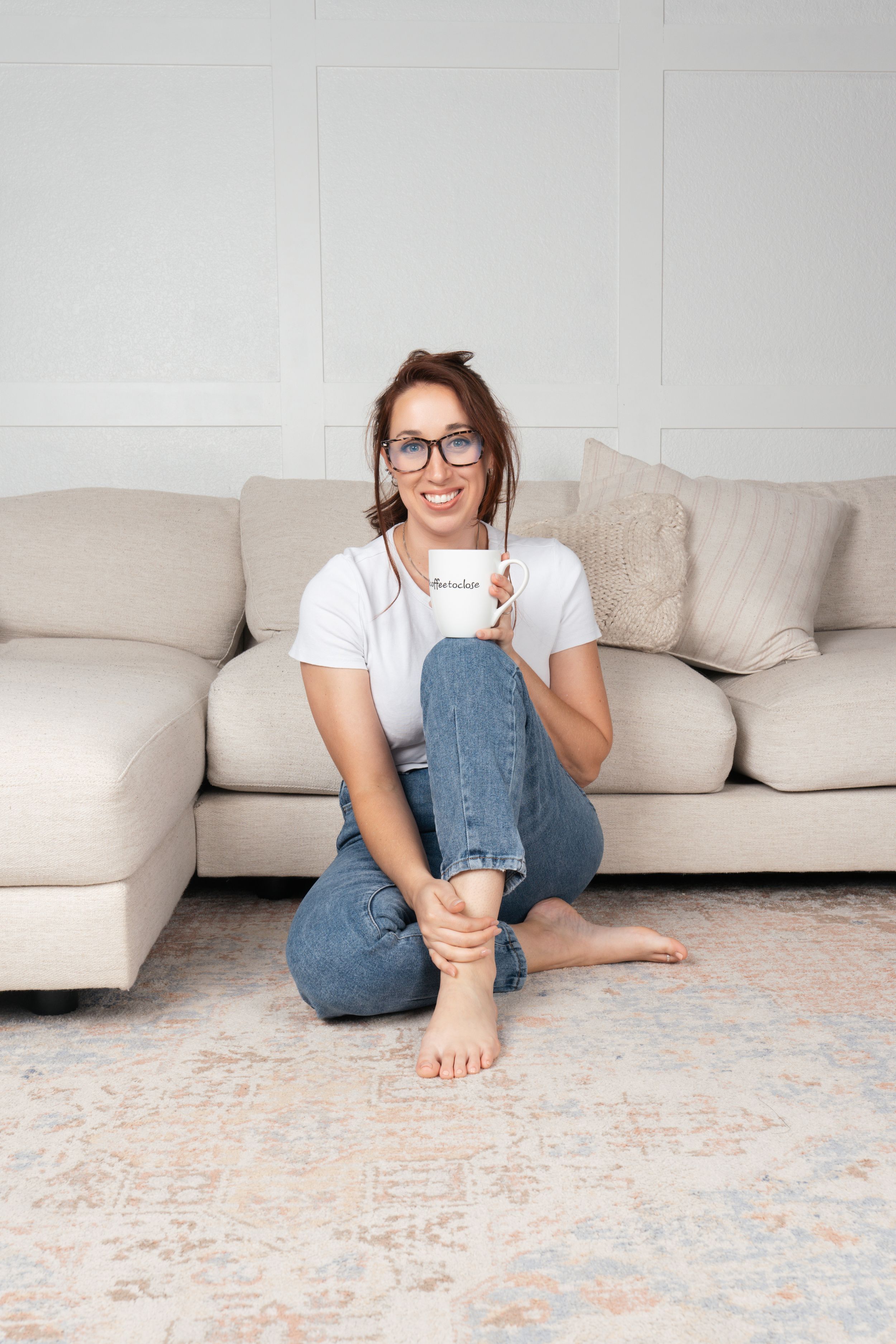 Casual portrait of person relaxing on floor with coffee cup wearing jeans and white t-shirt.