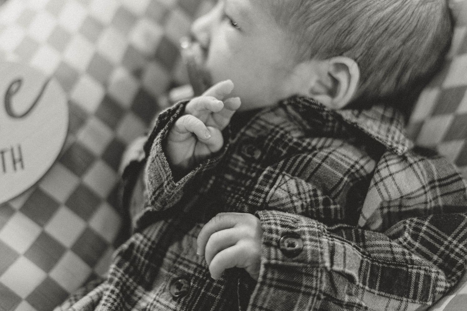 Black and white image of a child sleeping peacefully while wearing a plaid flannel shirt.
