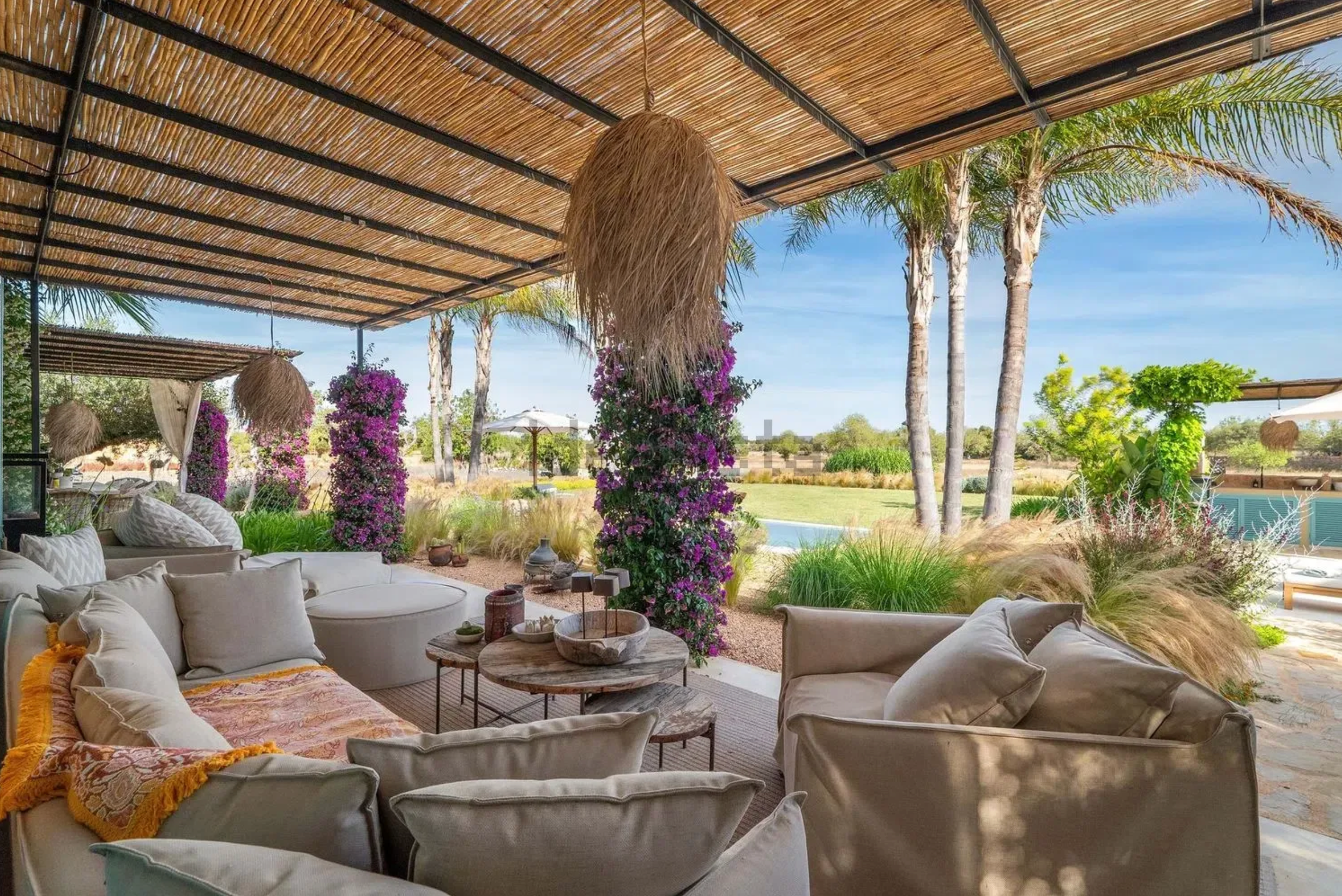 Luxurious beachfront lounge area with bamboo ceiling, white cushioned seating, and tropical palm trees swaying in the breeze.