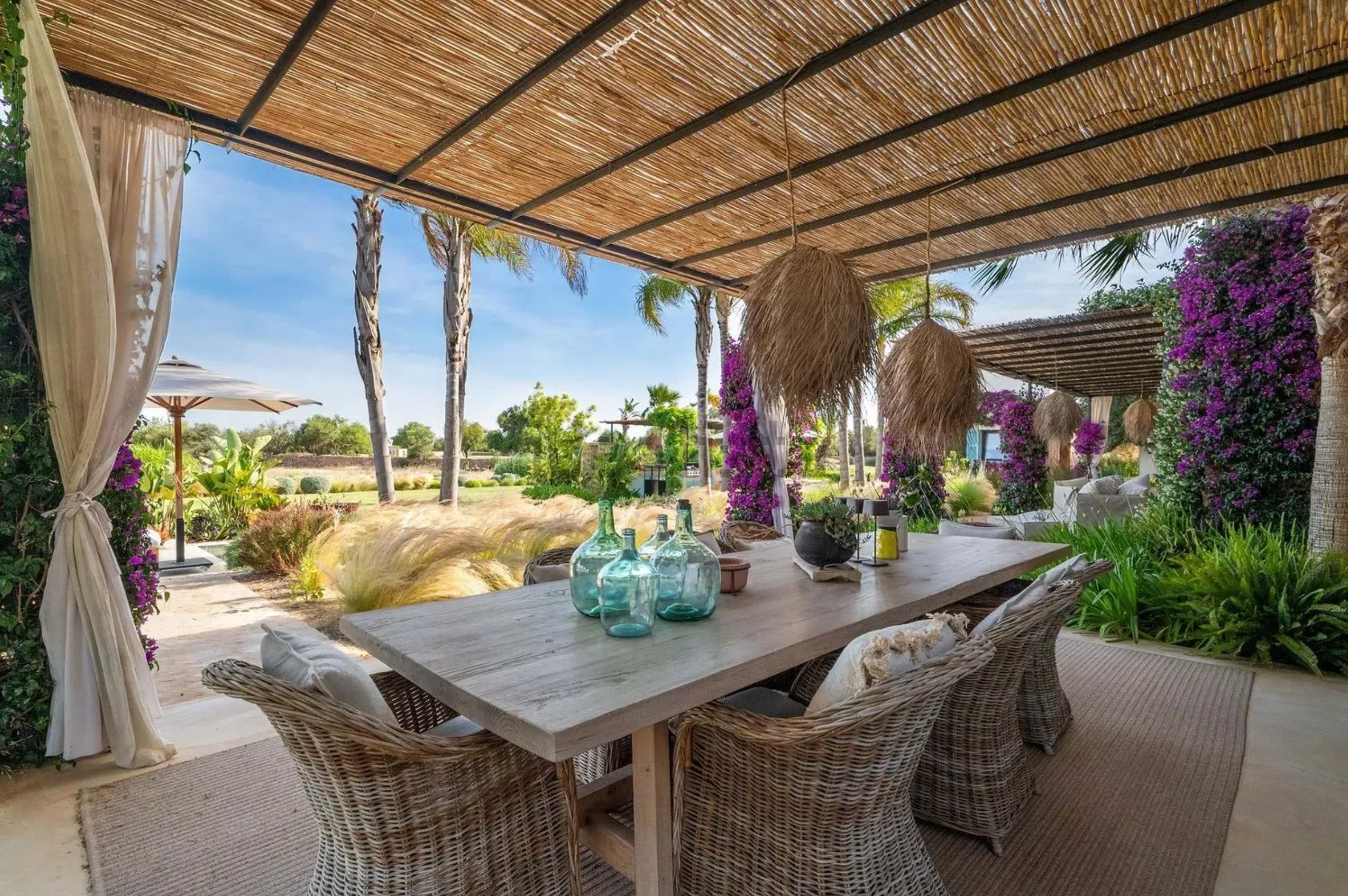 Luxurious outdoor patio space with bamboo ceiling, woven furniture, and purple bougainvillea flowers creating a tropical ambiance.