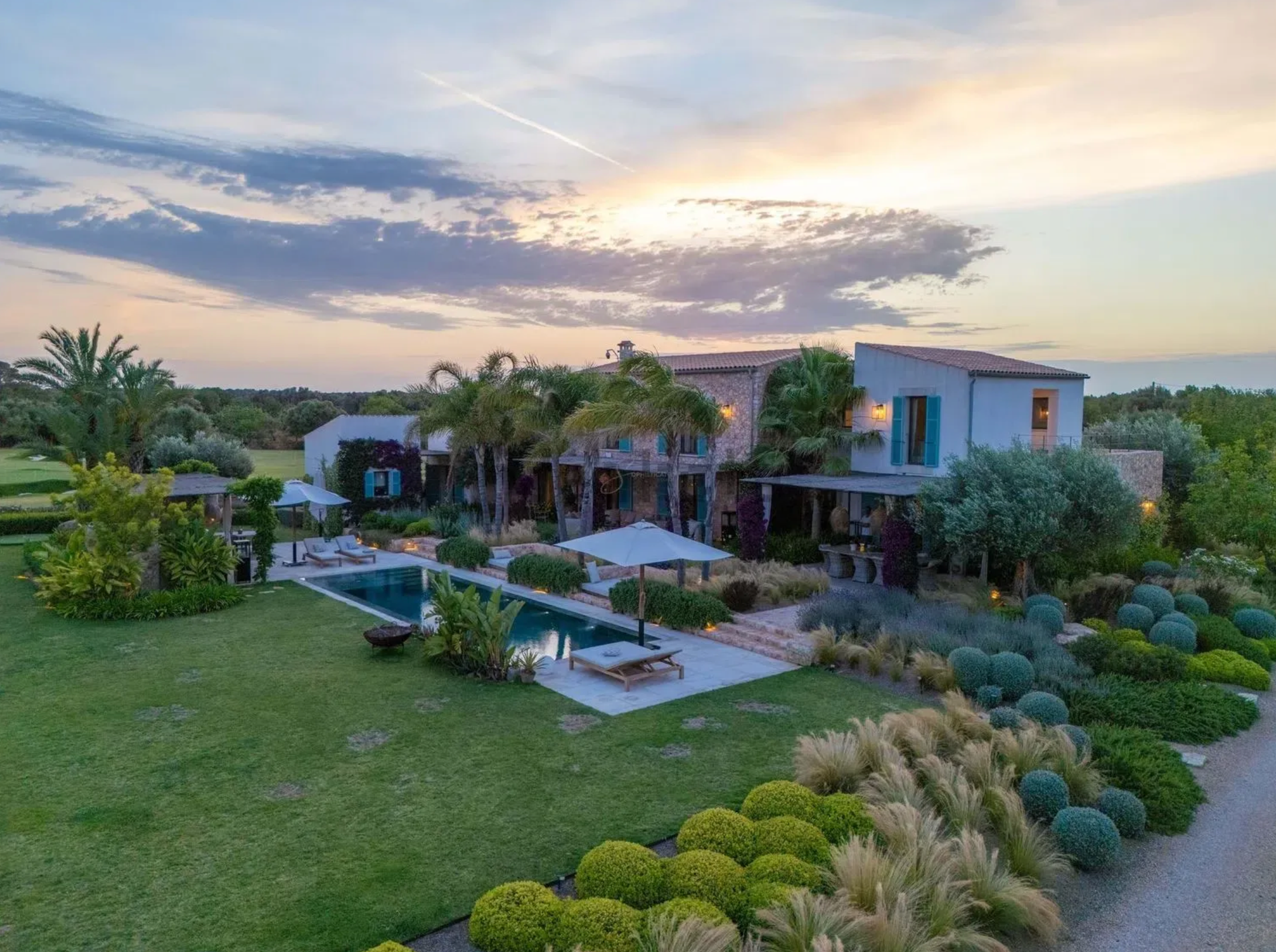 Panoramic view of a luxury Mediterranean villa with palm trees and manicured gardens at sunset.