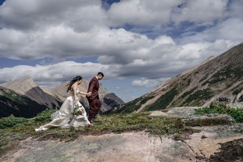 Couple walking along a mountain trail with dramatic cloudy skies and rocky peaks in Banff National Park.