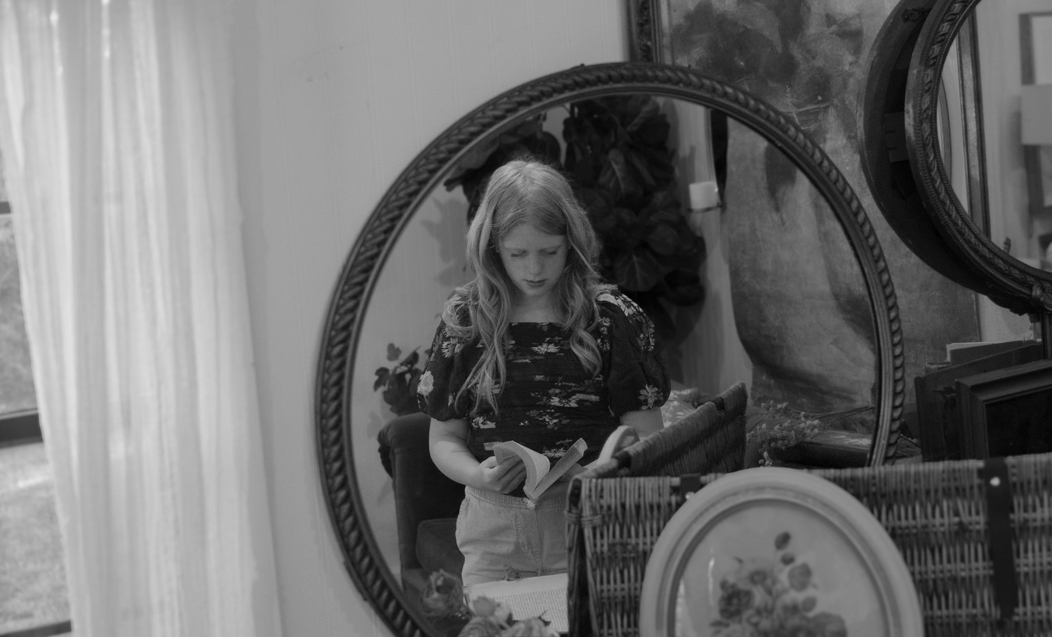 Collection of framed photographs displayed against white curtains in interior setting.
