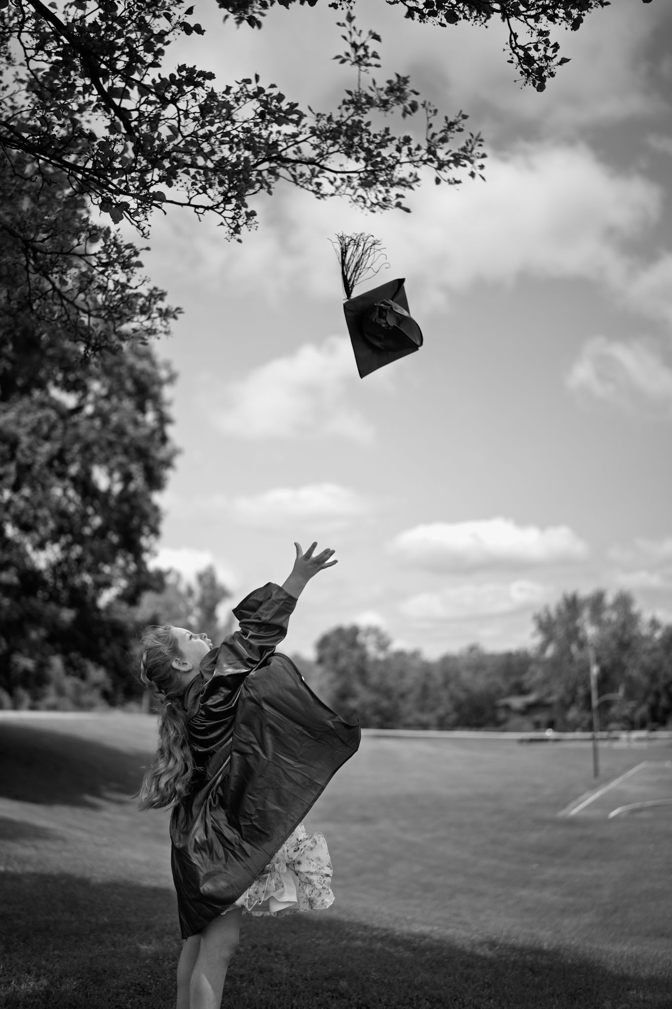 Black and white photo of graduate tossing cap in the air on a grassy hill.