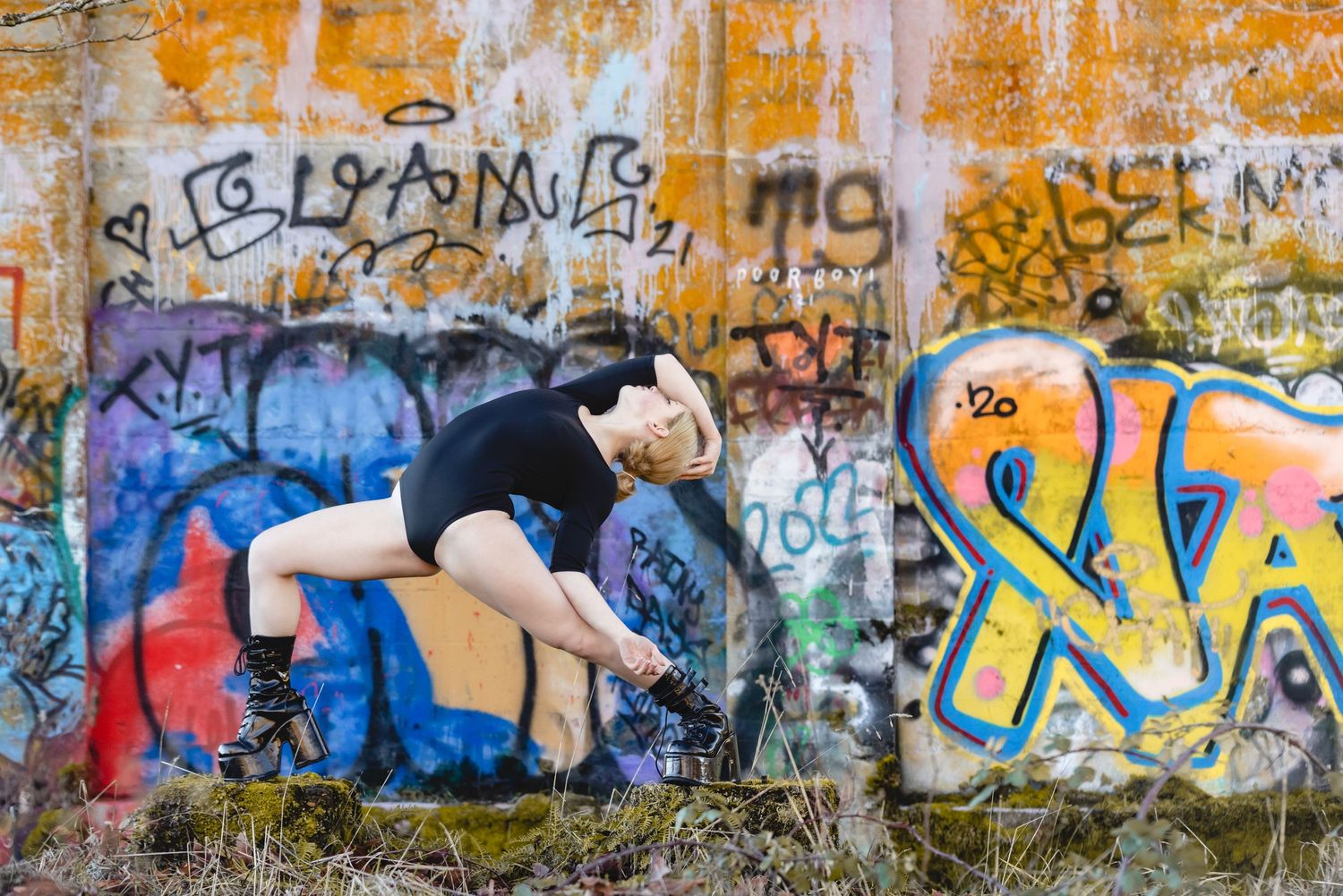 A person in black clothing crouches while spray painting graffiti art on a wall covered in colorful street art.