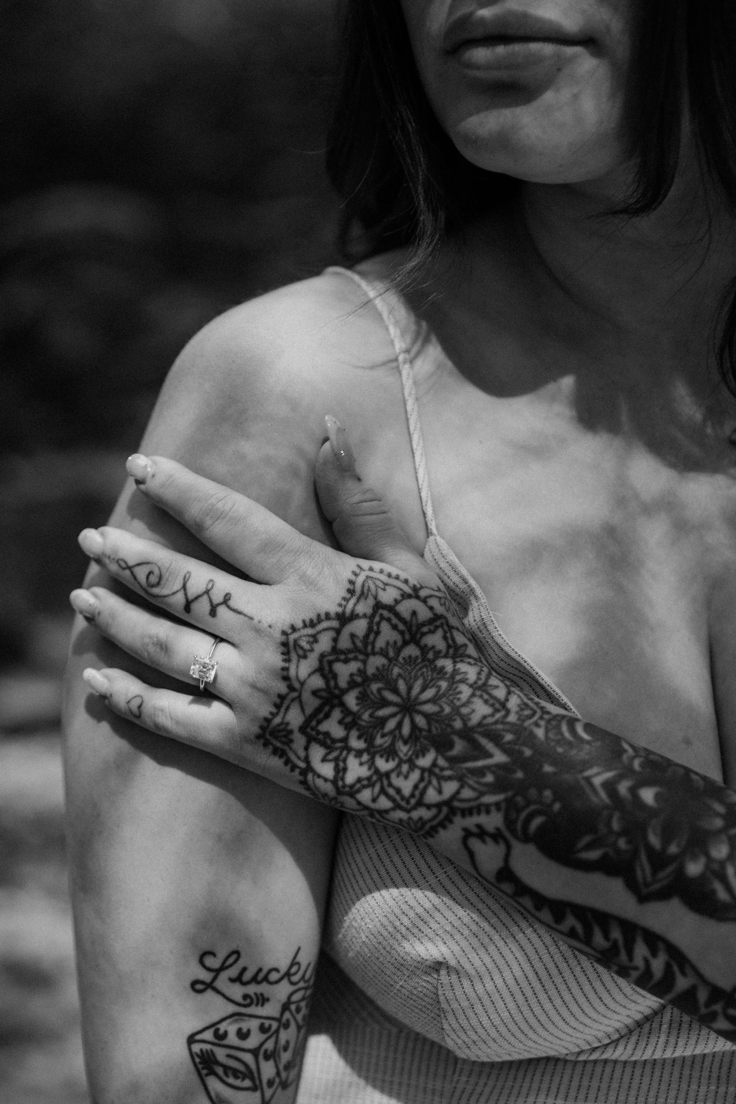 Black and white photo showing intricate mandala henna design on arm and hand with visible tattoo and jewelry ring.