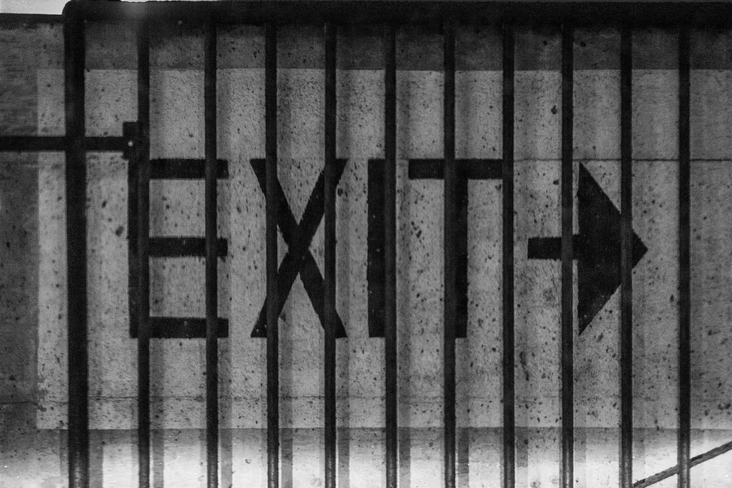 Black and white photograph of EXIT sign with arrow pointing right on a textured concrete wall.
