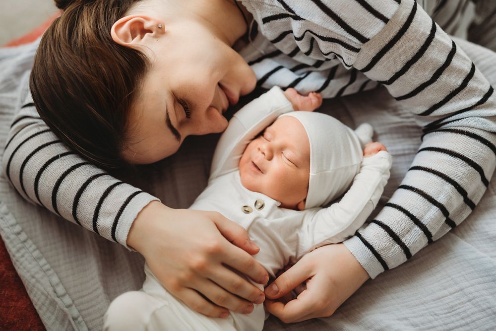 A person in striped shirt lying down next to a sleeping newborn baby in white onesie.