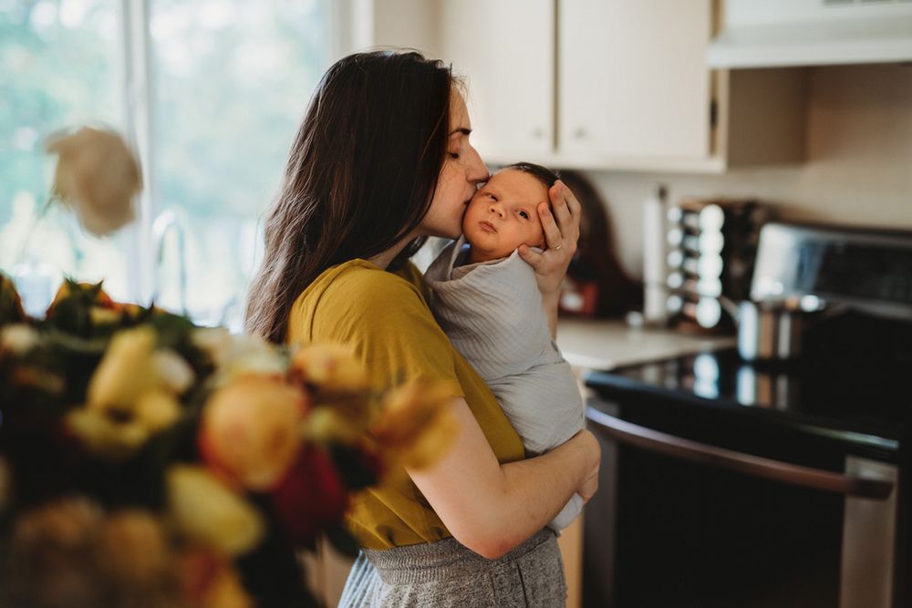 A heartwarming embrace shared between parent and baby in a sunlit kitchen with fruit in the background.