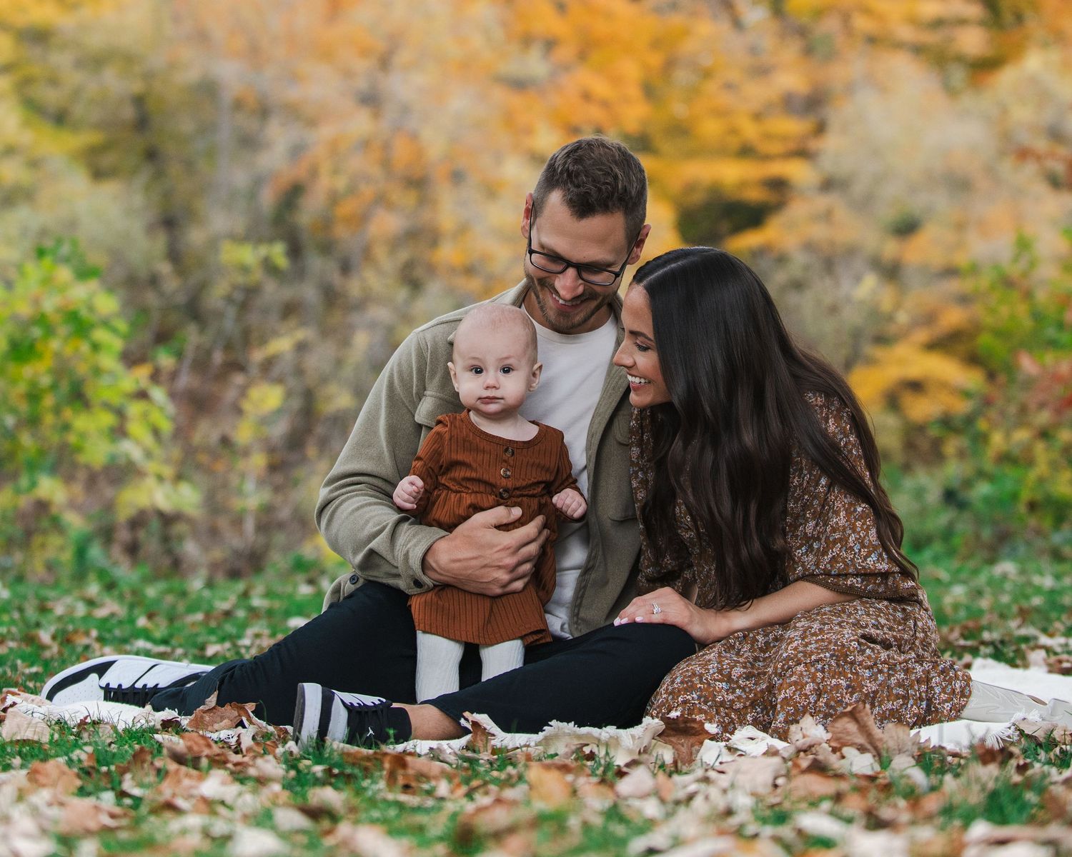 Four young people sitting together on rustic stone steps in an autumn forest setting during an outdoor photo session.