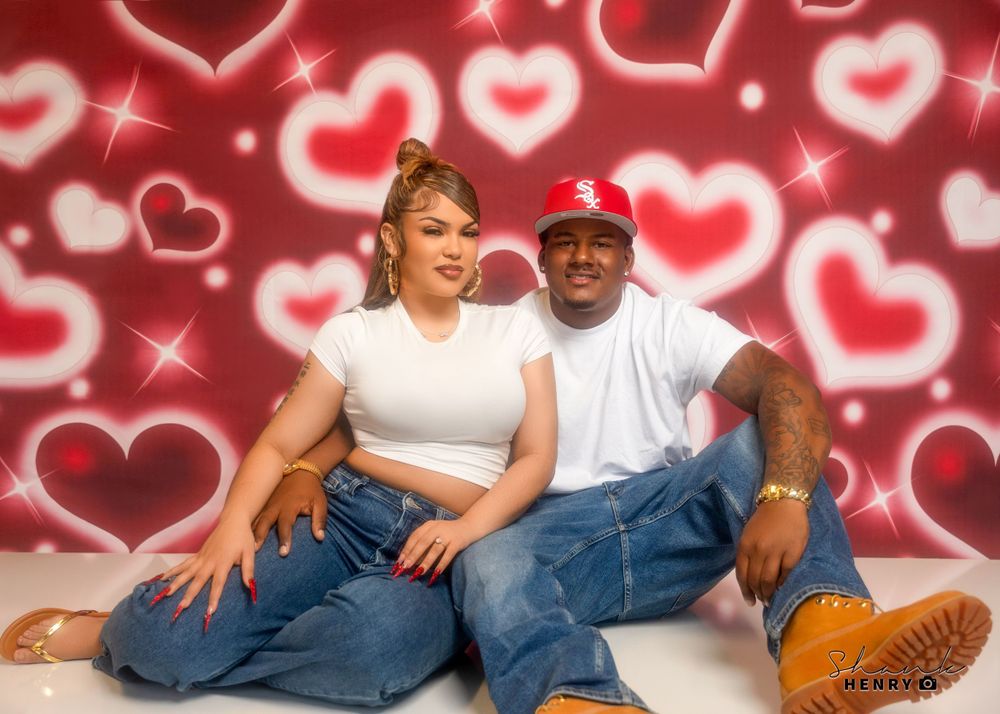 Couple poses for Valentine's themed photo against red background with floating heart graphics.