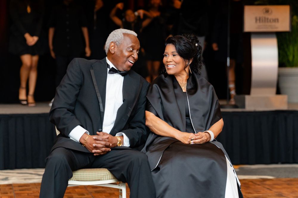 Two people in formal evening wear share a candid moment while seated at a Hilton event.