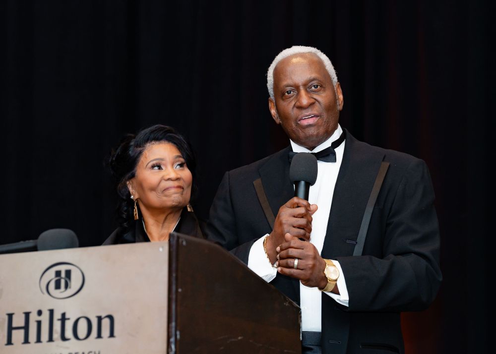 Two people in formal attire speak at a podium during an event at the Hilton.