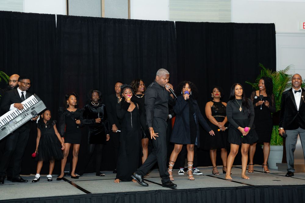 Group of formally dressed people stand in line on stage at an elegant black-tie event.