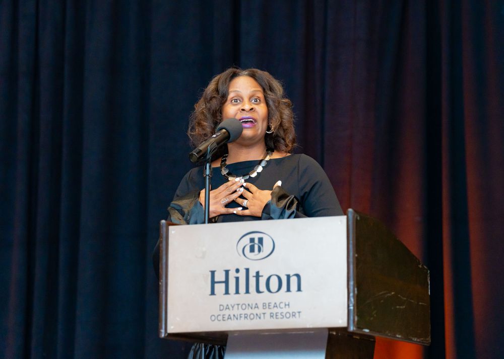 Speaker at Hilton podium delivers remarks during formal evening event.