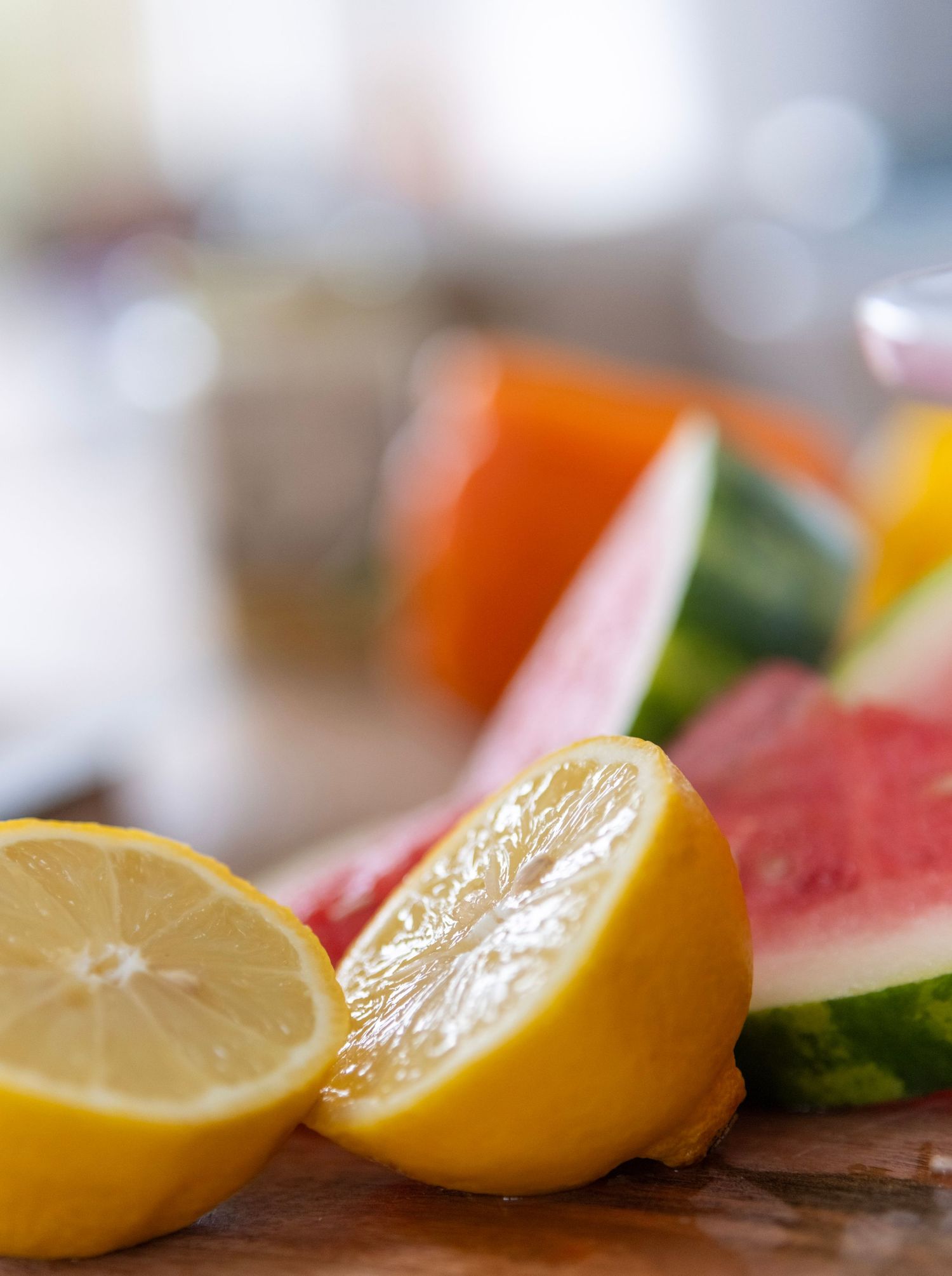 Fresh cut citrus fruits and watermelon slices on wooden cutting board with soft focus background.