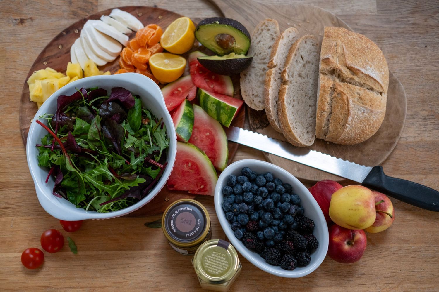 Healthy spread of fresh fruits, vegetables, bread, and blueberries arranged on wooden cutting board.