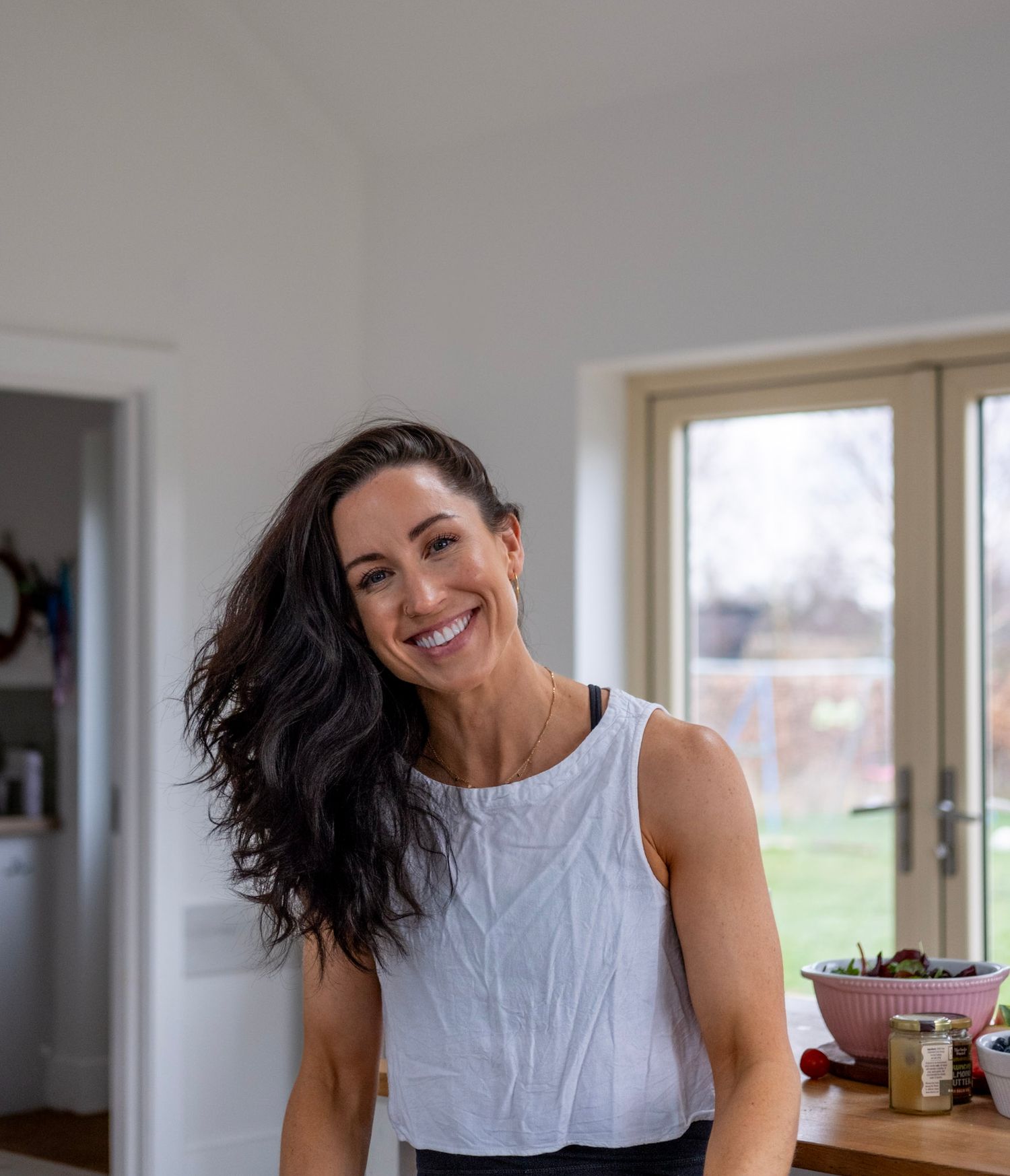 Person in white tank top smiling in bright kitchen setting.