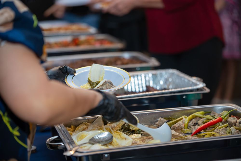 Buffet line with steam trays of food being served at a catering event.
