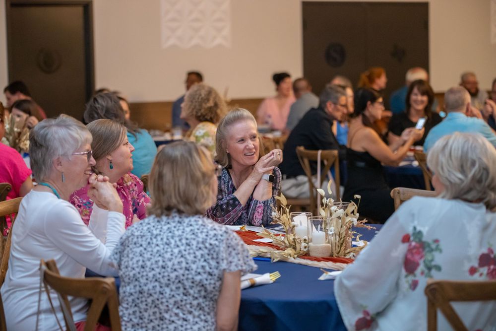 Large dining room filled with people seated at round tables for a community gathering.