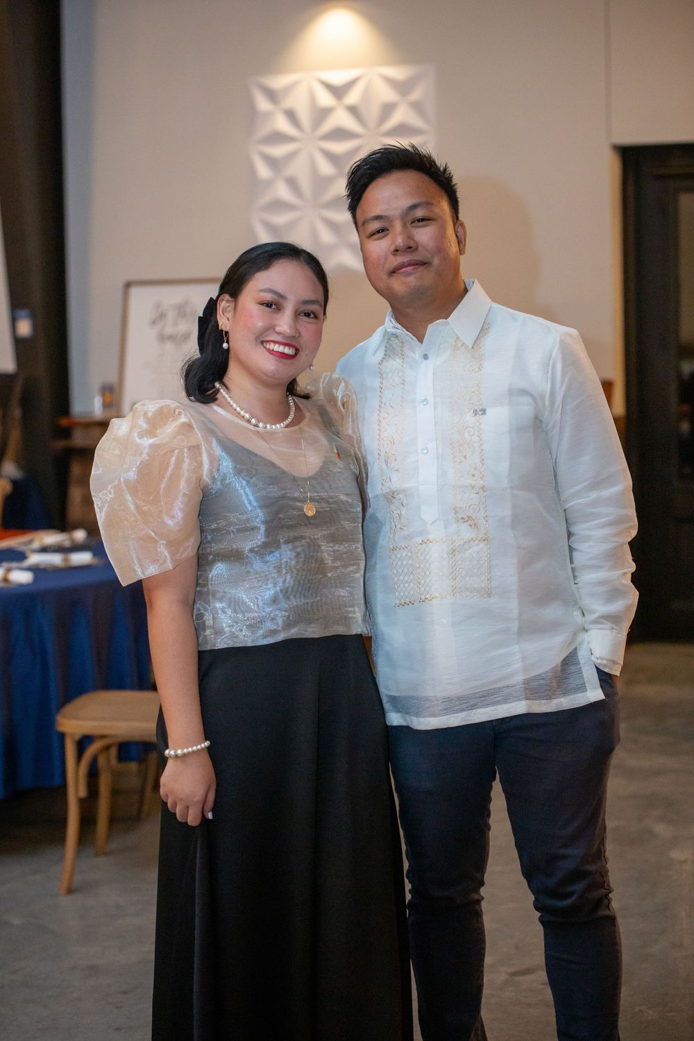 A couple poses together at an indoor event wearing coordinated white and black formal attire.