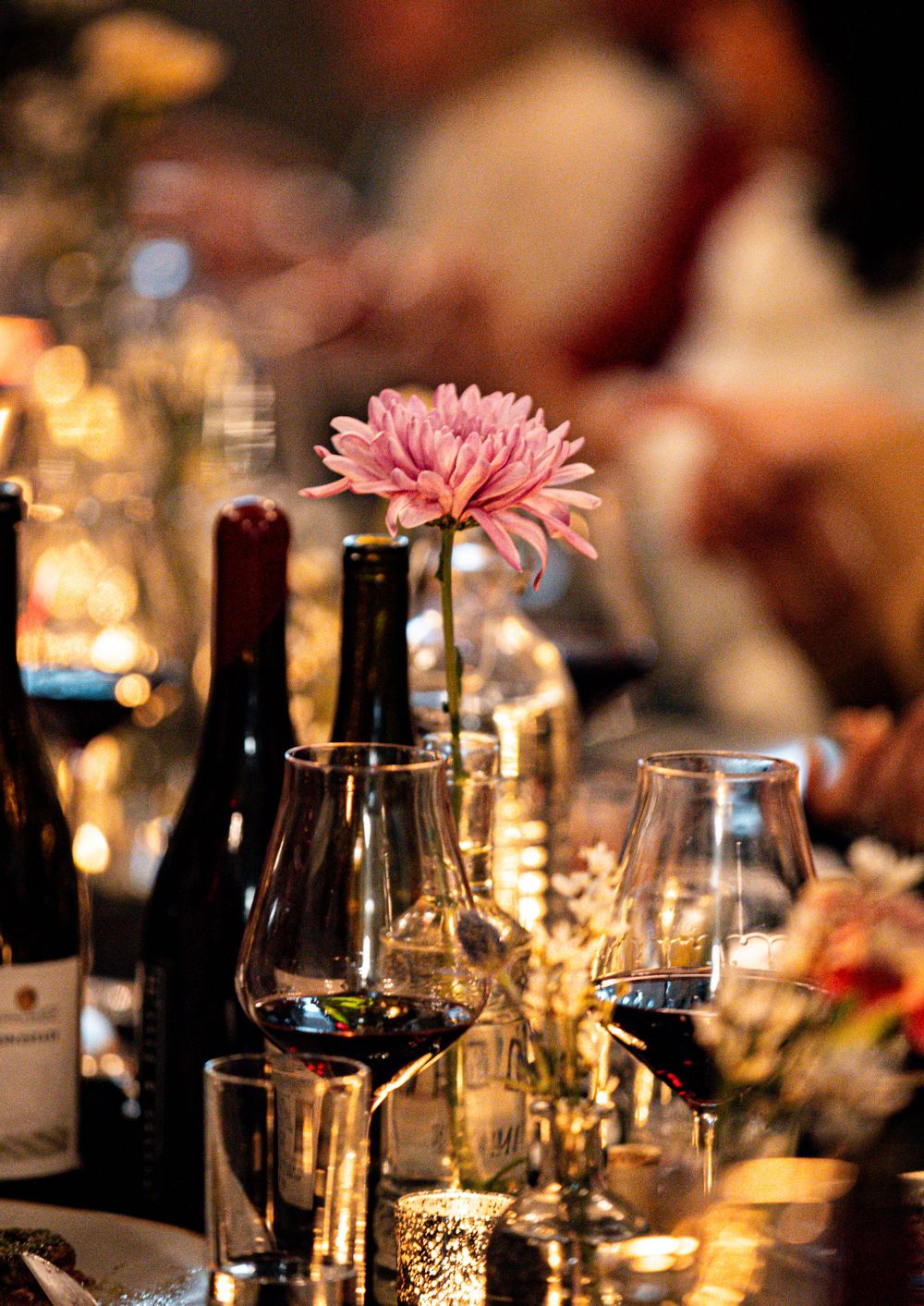 Elegant table setting with pink flowers, wine bottles and candlelight creating romantic ambiance.