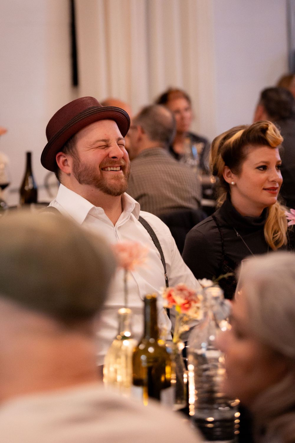 Guests enjoying a lively dinner party with wine bottles and table settings visible in the background.
