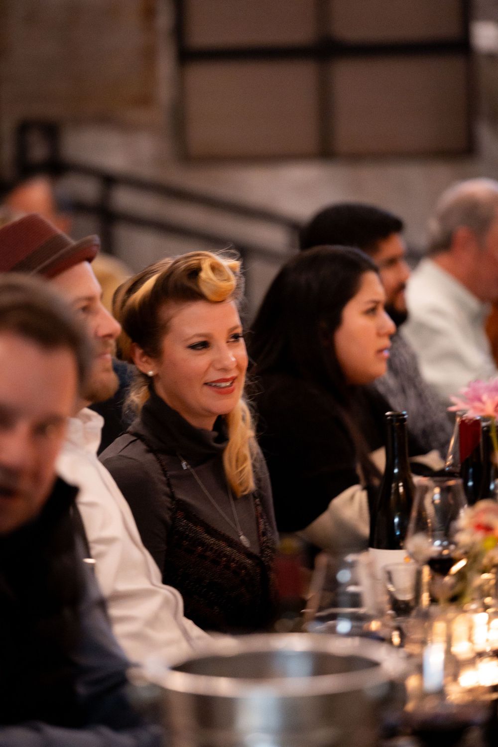 Diners seated at a long table with vintage-style decor and wine bottles.