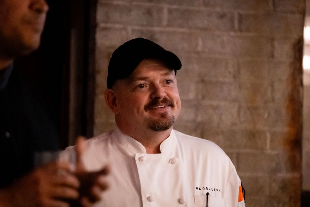 A chef in white uniform and baseball cap at a social gathering.