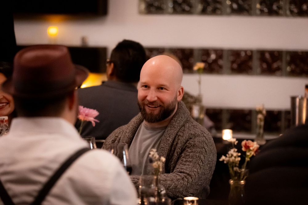 Guests enjoying conversation at a casual dinner gathering with ambient lighting.